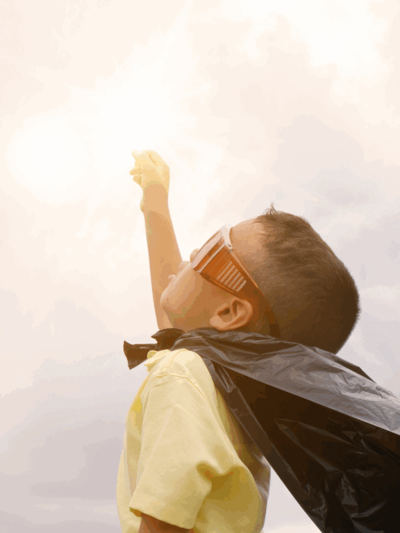 Sonnenschein hinter einem Jungen mit Sonnenbrille, der nach oben zeigt, symbolisiert Optimismus und Zukunftsaussichten, passend für astrologische und spirituelle Themen.