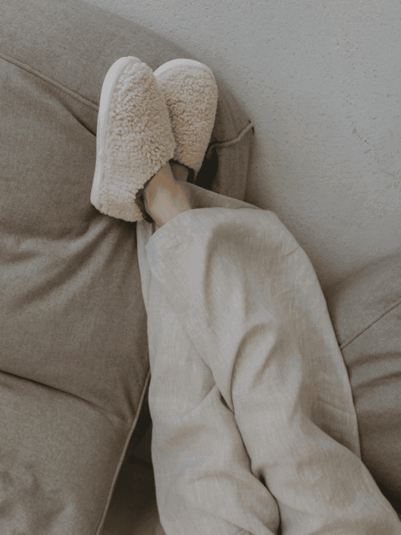 Komfortable Hausschuhe auf dem Sofa, gemütliche Entspannungsmomente, bequeme Wohnzimmerkleidung, Wohlfühlatmosphäre, entspannte Freizeitbeschäftigung, kuschelige Hausschuhe.